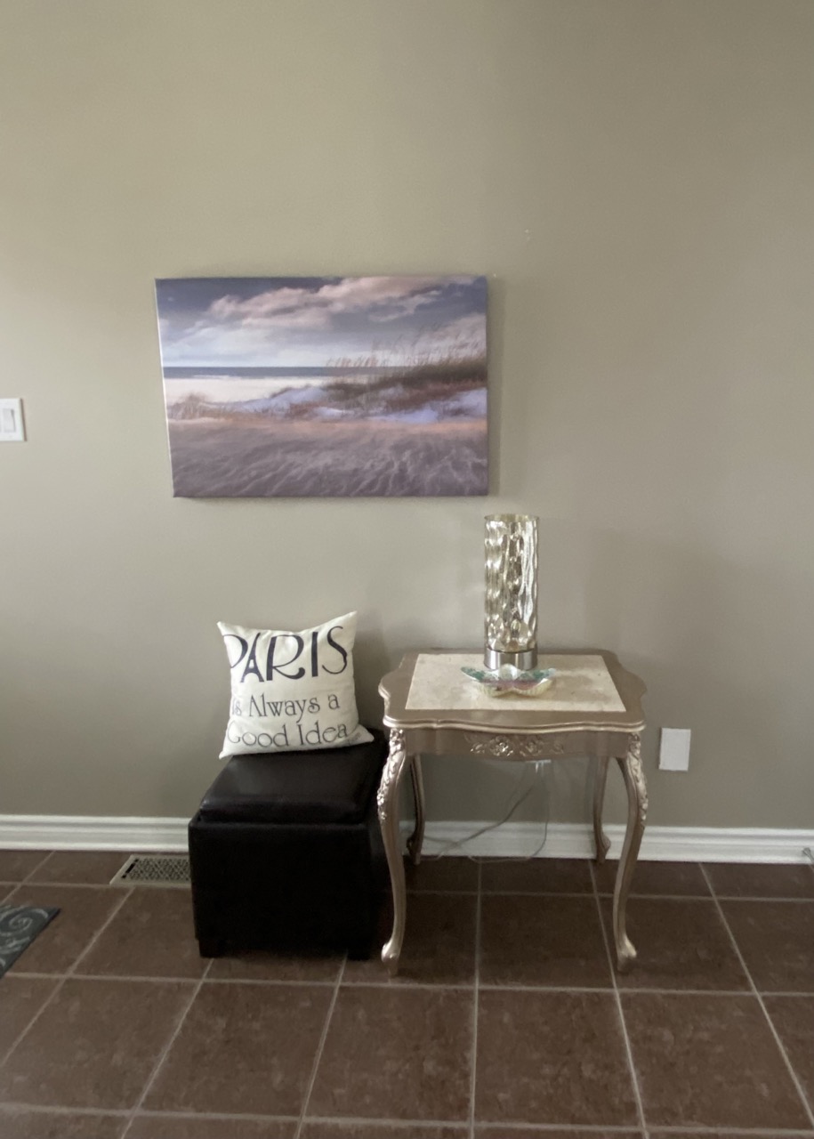 image of front entry before showing small table and stool and art on wall