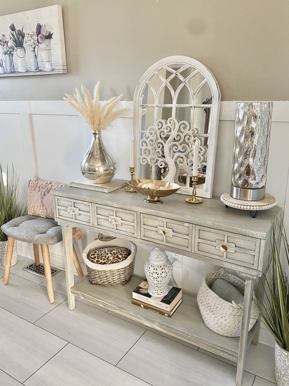 reveal image of DIY front entryway ideas showing side view of grey table with drawers, flowers and a mirror on top and a stool beside it