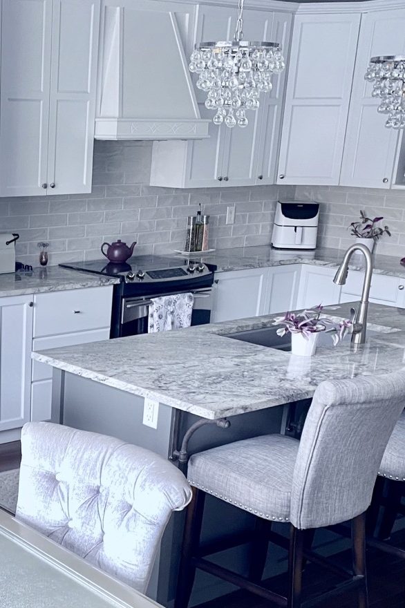image of kitchen cabinet makeover showing white painted kitchen cabinets  with crystal pendants over the deep grey painted island