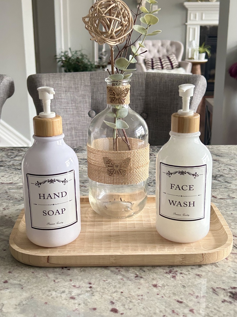 reveal image of easy DIY soap bottle project showing white soap bottles on a bamboo tray with vase of eucalyptus